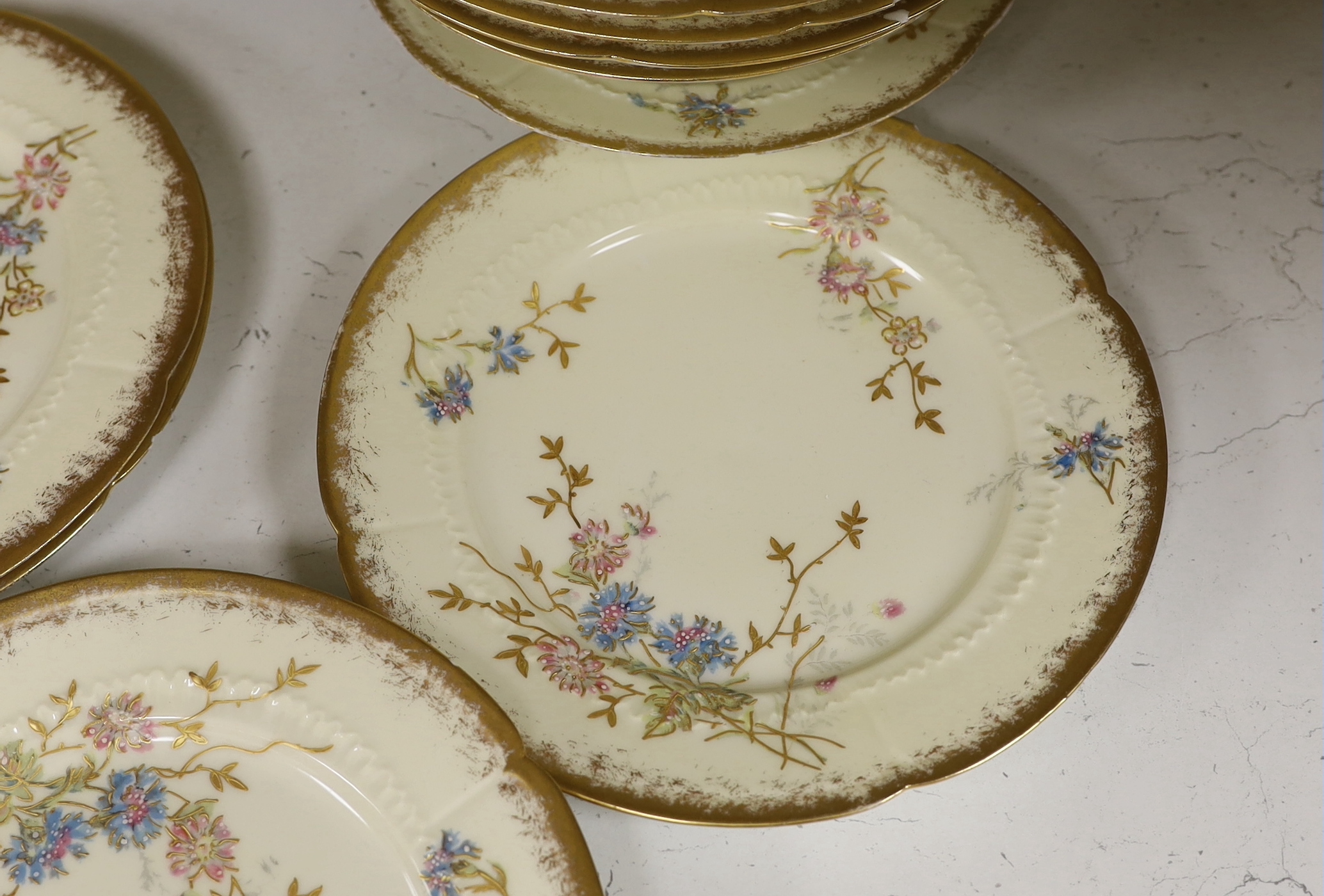 Thirteen Limoges style porcelain dessert plates, two on pedestal bases, gilt decorated with cornflowers etc., 24.5cm diameter
